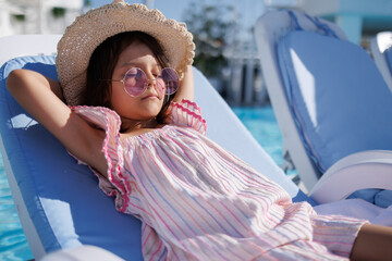 Funny little girl relaxing on summer vacation. The child has fun on the beach. Cute baby in a colorful swimsuit and sunglasses is resting.