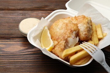 British Traditional Fish and chips with lemon and sauce on wooden table, closeup