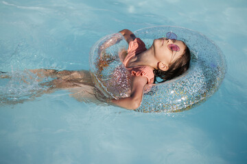 Cute funny toddler girl in a sunglasses relaxing on inflatable toy ring floating in pool have fun during summer vacation. Child having fun in swimming pool.