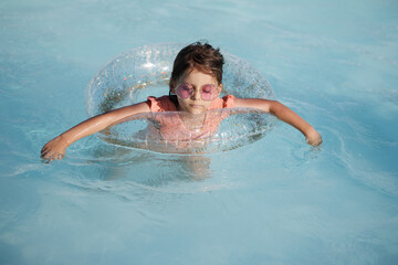 Cute funny toddler girl in a sunglasses relaxing on inflatable toy ring floating in pool have fun during summer vacation. Child having fun in swimming pool. 