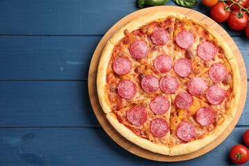 Delicious pepperoni pizza, fresh tomatoes and basil on blue wooden table, flat lay. Space for text