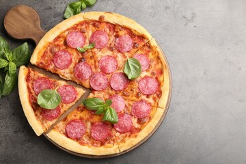 Delicious cut pepperoni pizza with fresh basil on grey table, top view. Space for text