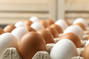 Many raw chicken eggs in carton indoors, closeup