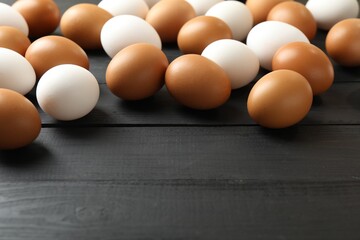 Many raw chicken eggs on black wooden table, closeup. Space for text