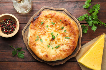 Delicious Megrelian khachapuri with ingredients on wooden table, flat lay