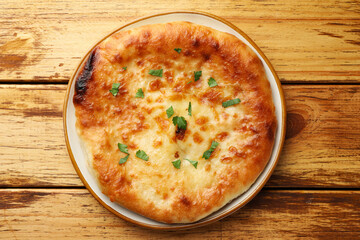 Delicious Megrelian khachapuri with parsley on wooden table, top view