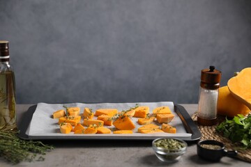 Pieces of fresh pumpkin with thyme and other spices on grey table