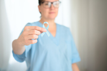 Close up of female medical worker in uniform with blue ribbon on hand. Prostate cancer awareness,...