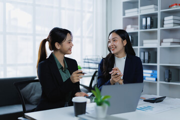 Fototapeta premium Asian businesswomen are engaging in a productive discussion, exchanging ideas and collaborating while working together at a desk in a bright, contemporary office environment