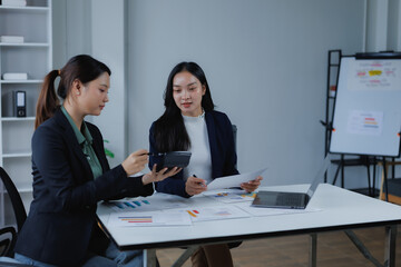 Two businesswomen collaborating on financial data, discussing quarterly results and reviewing documents, charts, and using a calculator during a professional meeting in an office setting