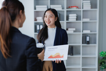 Two professional Asian businesswomen reviewing and discussing Analyze Selling Product chart data, collaborating on business strategy in a modern office setup