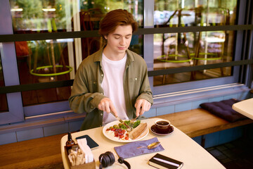 Young man enjoys a delicious meal in a modern cafe while seated at a sunny table