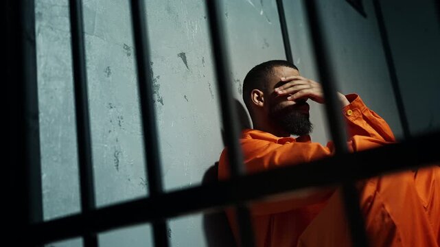 African American inmate sitting on floor behind bars, feeling regret and remorse