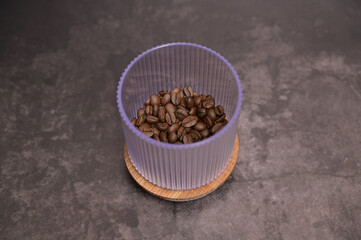 Dark roasted coffee beans in a transparent glass on a wooden board. Dark background. Still Life. Place for adding text, menu, design