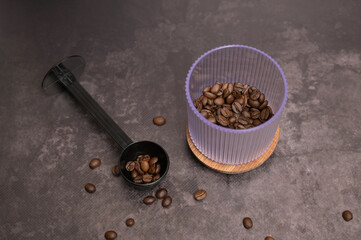 Dark roasted coffee beans in a transparent glass on a wooden board with a black spoon on the side. Dark background. Still life. Place for adding text, design