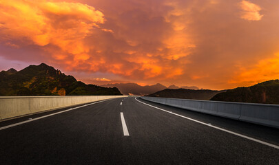 Asphalt highway road and mountain landscape under a spectacular orange sky at sunset