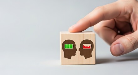 Mental Health in the workplace, A hand holds a block depicting two heads, one with a full battery symbol and the other with a declining chart, emotional mental energy.