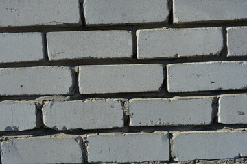Construction and renovation work, a wall with imperfections and unevenness, the first masonry. A wall of white brick, gray cement, illuminated by the rays of the sun.