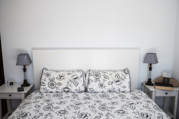 One bedroom with double bed. It has two white wooden tables and on one of them a book with a pair of glasses. White decoration