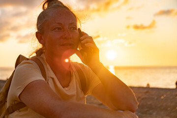 Woman enjoying sunset at the beach while talking on her phone and taking in the beautiful view