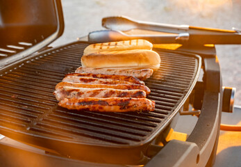 Grilling sausages and a bun outdoors during golden hour on a warm summer evening
