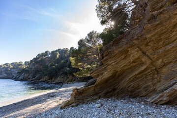 Discover a secluded pebble beach with stunning rock formations and lush greenery, bathed in the warm glow of the sun for your next adventure