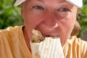 Woman enjoying a delicious wrap filled with fresh ingredients in a sunny outdoor setting
