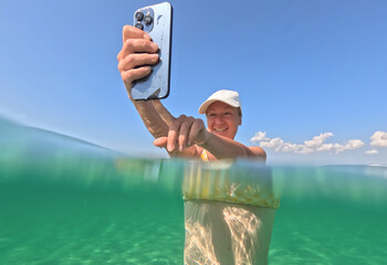 A happy woman with a smartphone standing in clear turquoise sea water under a bright blue sky in a sunny outdoor setting. A female tourist booking air tickets using a mobile phone app in Travel