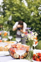 Summer picnic table outdoors decorated with flowers and blurred photographer.