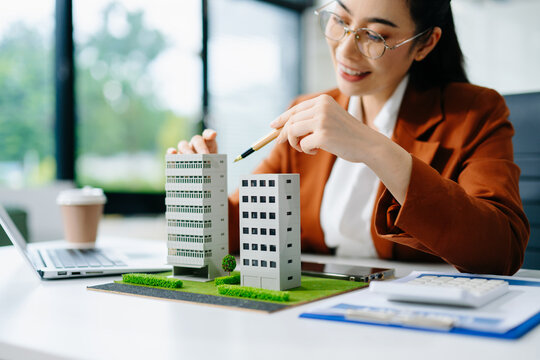 Confident businesswoman analyzing building models at office desk. Perfect for real estate, property investment, mortgage planning, and corporate finance themes.