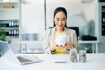 Smiling Asian businesswoman holding white piggy bank. Concept of finance, savings, investment, and...