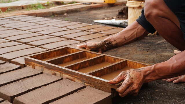 Handmade Mud Bricks Process, focusing on a worker's hands covered in slurry removing the wooden mold from the wet clay.