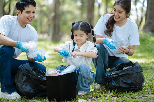 Asian family collects plastic bottles into black bags at a park on the weekend. - Powered by Adobe