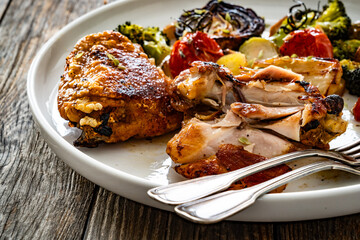 Roasted chicken thighs with grilled vegetables on wooden table	