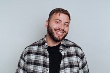 Fototapeta premium Smiling man wearing a plaid shirt poses for a friendly portrait against a light background