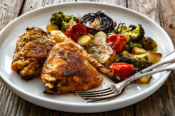 Roasted chicken thighs with grilled vegetables on wooden table	