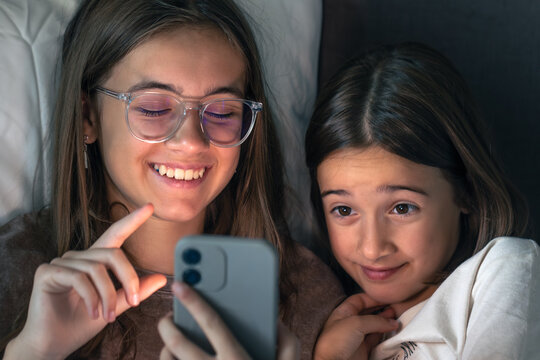 Girls laugh at phone content with warm screen light and cuddles. Friendship, laugh, wow moment.
