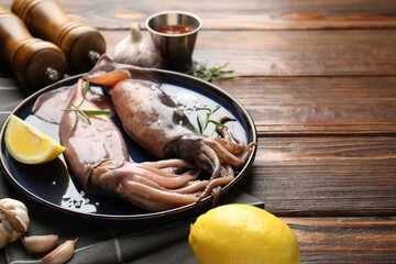 Raw squids, lemon and rosemary on wooden table, closeup. Space for text