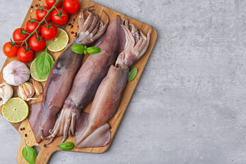 Fresh raw squids, tomatoes, lime slices and spices on grey table, top view. Space for text