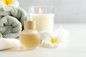 Essential oil, towel, burning candles, plumeria flowers and spa stones on white table, closeup. Space for text