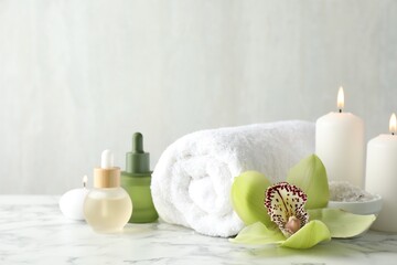 Beautiful spa composition with essential oils and burning candles on white marble table, closeup