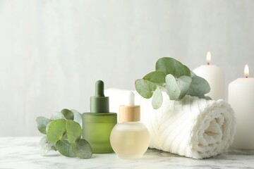 Beautiful spa composition with essential oils and burning candles on white marble table, closeup