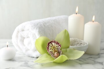 Beautiful spa composition with sea salt and burning candles on white marble table, closeup