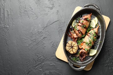 Tasty cooked squids with sauce and garlic in dish on black table, top view. Space for text