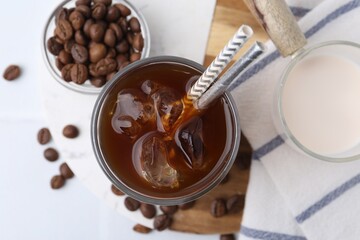 Tasty iced coffee, milk and beans on white table, flat lay