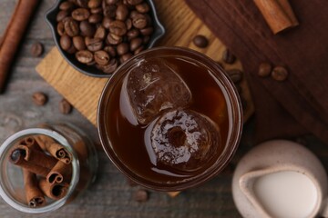 Tasty iced coffee, milk, cinnamon and beans on wooden table, flat lay