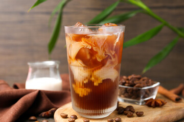Tasty iced coffee in glass, milk and beans on wooden table, closeup