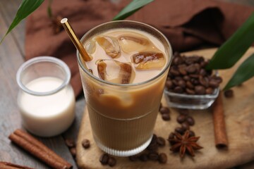 Tasty iced coffee in glass, milk and beans on wooden table, closeup