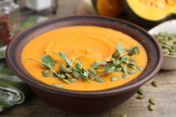 Delicious pumpkin soup with seeds and microgreens in bowl on wooden table, closeup