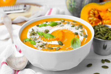 Delicious pumpkin soup with spices, cheese and sour cream in bowl served on table, closeup